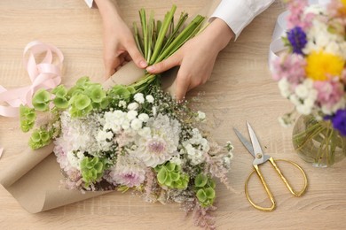 Photo of Florist making bouquet of flowers at wooden table, top view
