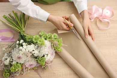 Photo of Florist making bouquet of flowers at wooden table, top view