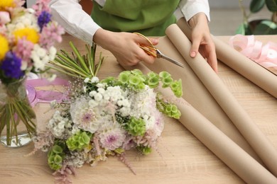 Photo of Florist making bouquet of flowers at wooden table, closeup