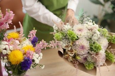 Photo of Florist making bouquet of flowers at table indoors, closeup