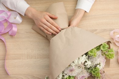 Photo of Florist making bouquet of flowers at wooden table, top view
