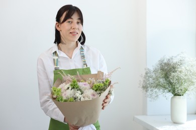 Photo of Florist with beautiful bouquet of flowers near white wall indoors