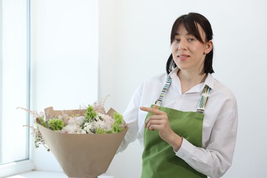 Photo of Florist with beautiful bouquet of flowers near window indoors