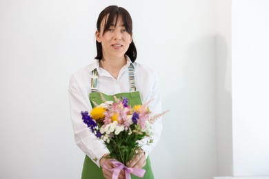 Photo of Florist with beautiful bouquet of flowers near white wall indoors