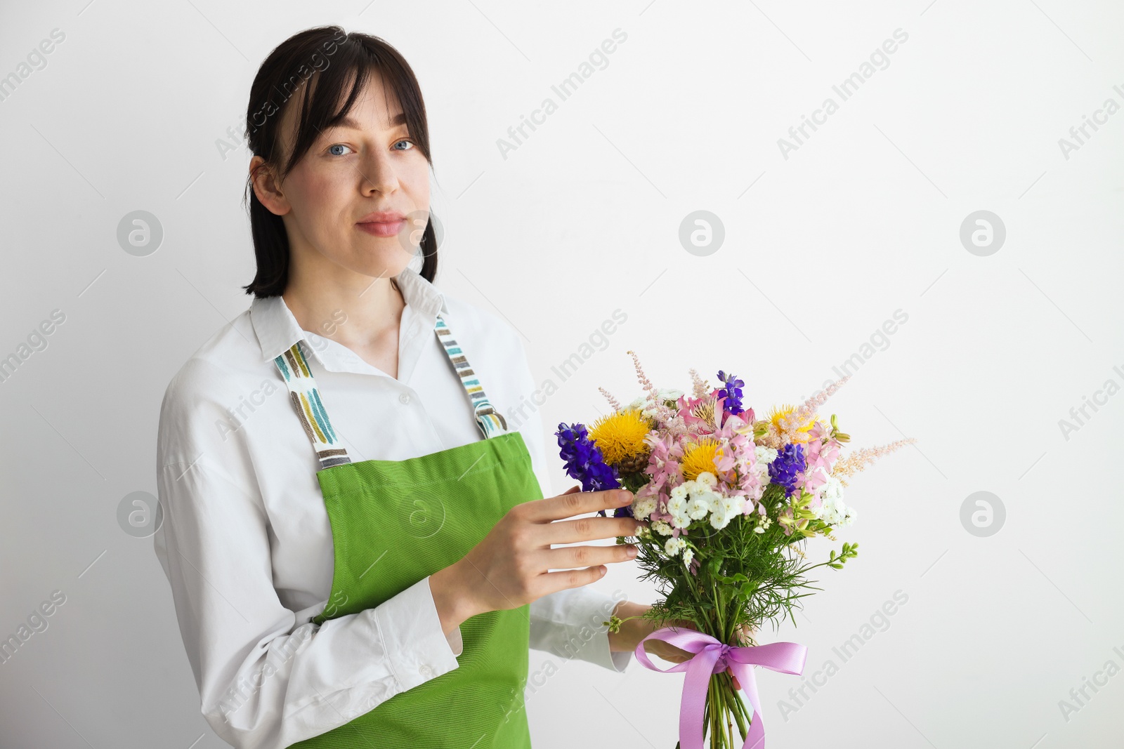Florist with beautiful bouquet of flowers near white wall indoors Photo of Florist with beautiful bouquet of flowers near white wall indoors