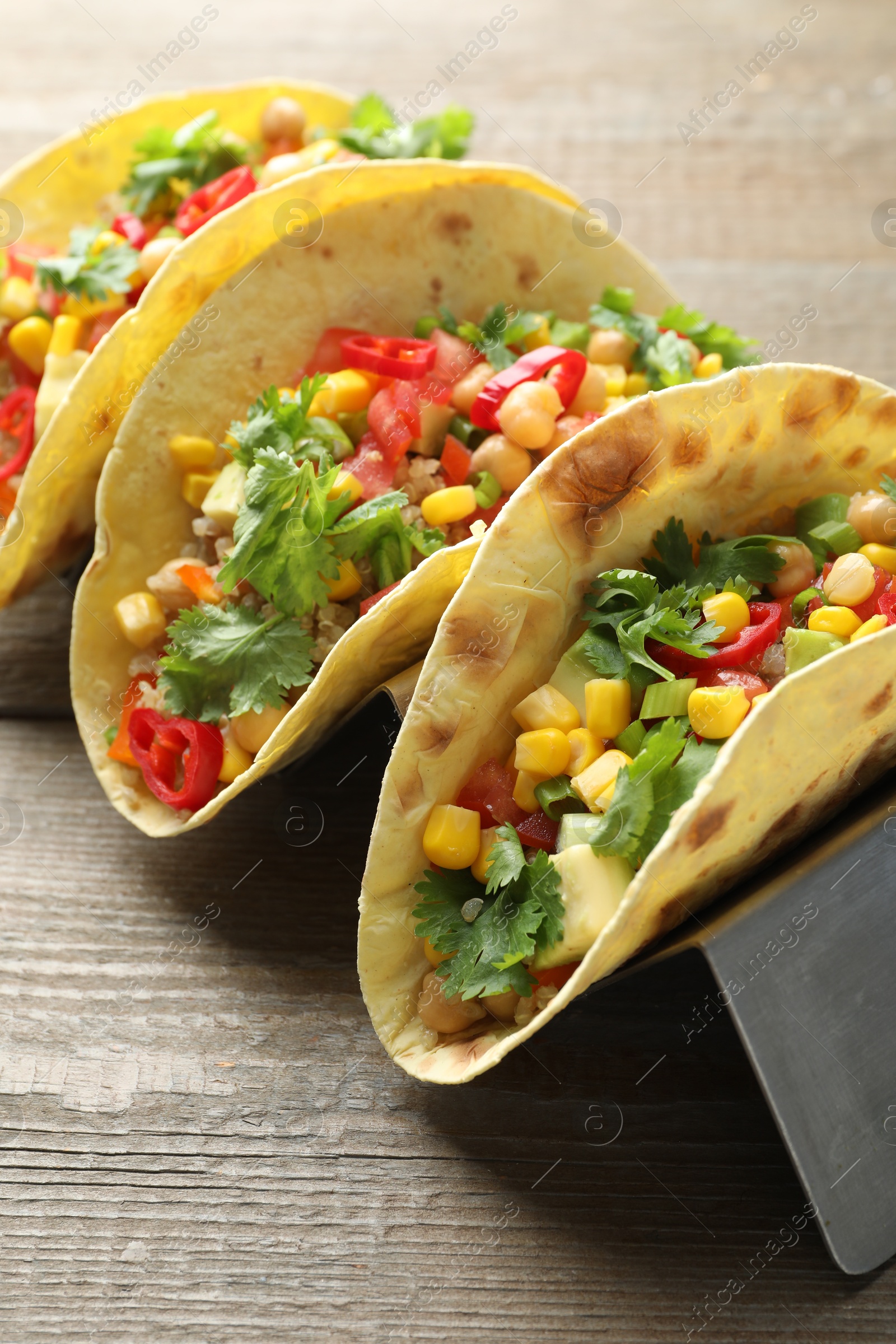 Photo of Tasty vegetarian tacos with chickpeas, corn and quinoa served on wooden table, closeup