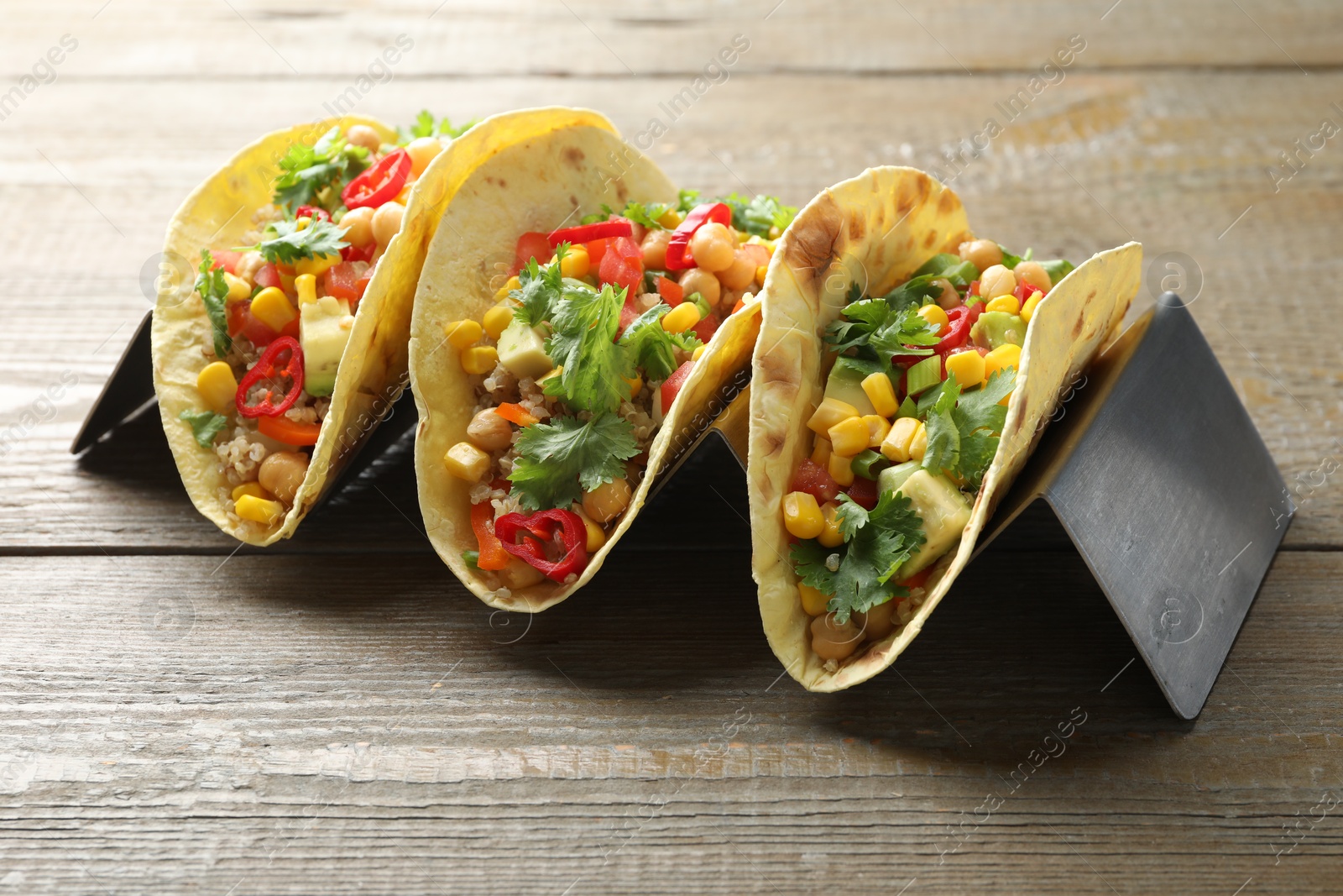 Photo of Tasty vegetarian tacos with chickpeas, corn and quinoa served on wooden table, closeup