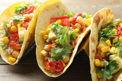 Photo of Tasty vegetarian tacos with chickpeas, corn and quinoa served on wooden table, closeup