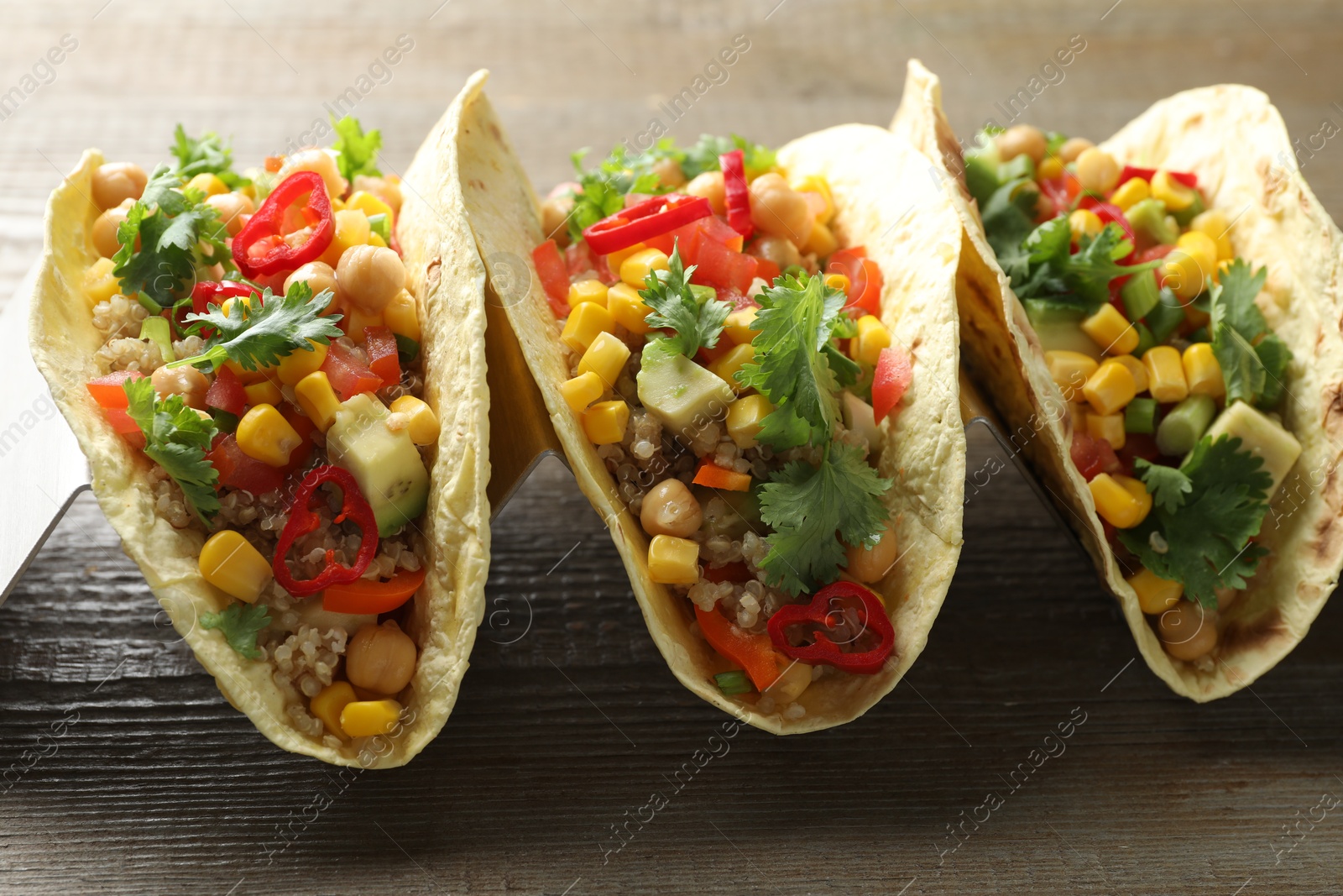 Photo of Tasty vegetarian tacos with chickpeas, corn and quinoa served on wooden table, closeup