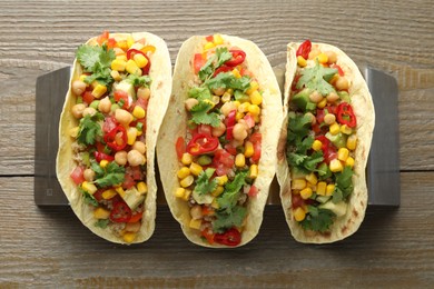 Photo of Tasty vegetarian tacos with chickpeas, corn and quinoa served on wooden table, top view