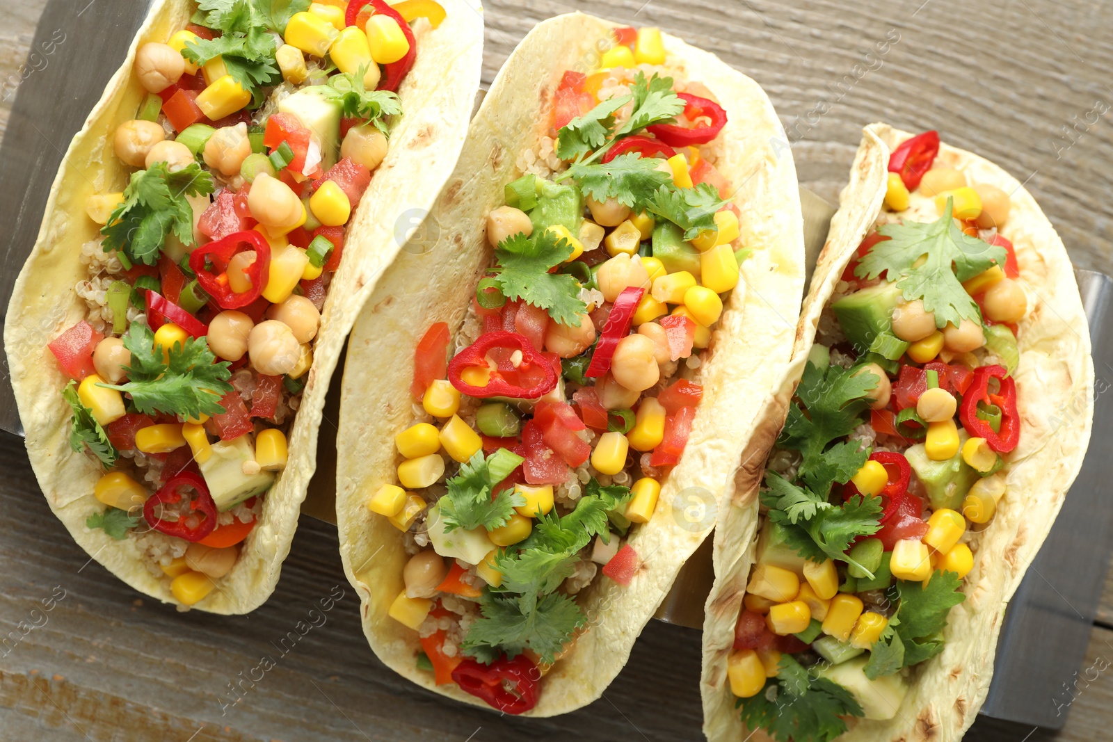 Photo of Tasty vegetarian tacos with chickpeas, corn and quinoa served on wooden table, top view