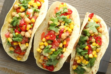 Photo of Tasty vegetarian tacos with chickpeas, corn and quinoa served on wooden table, top view