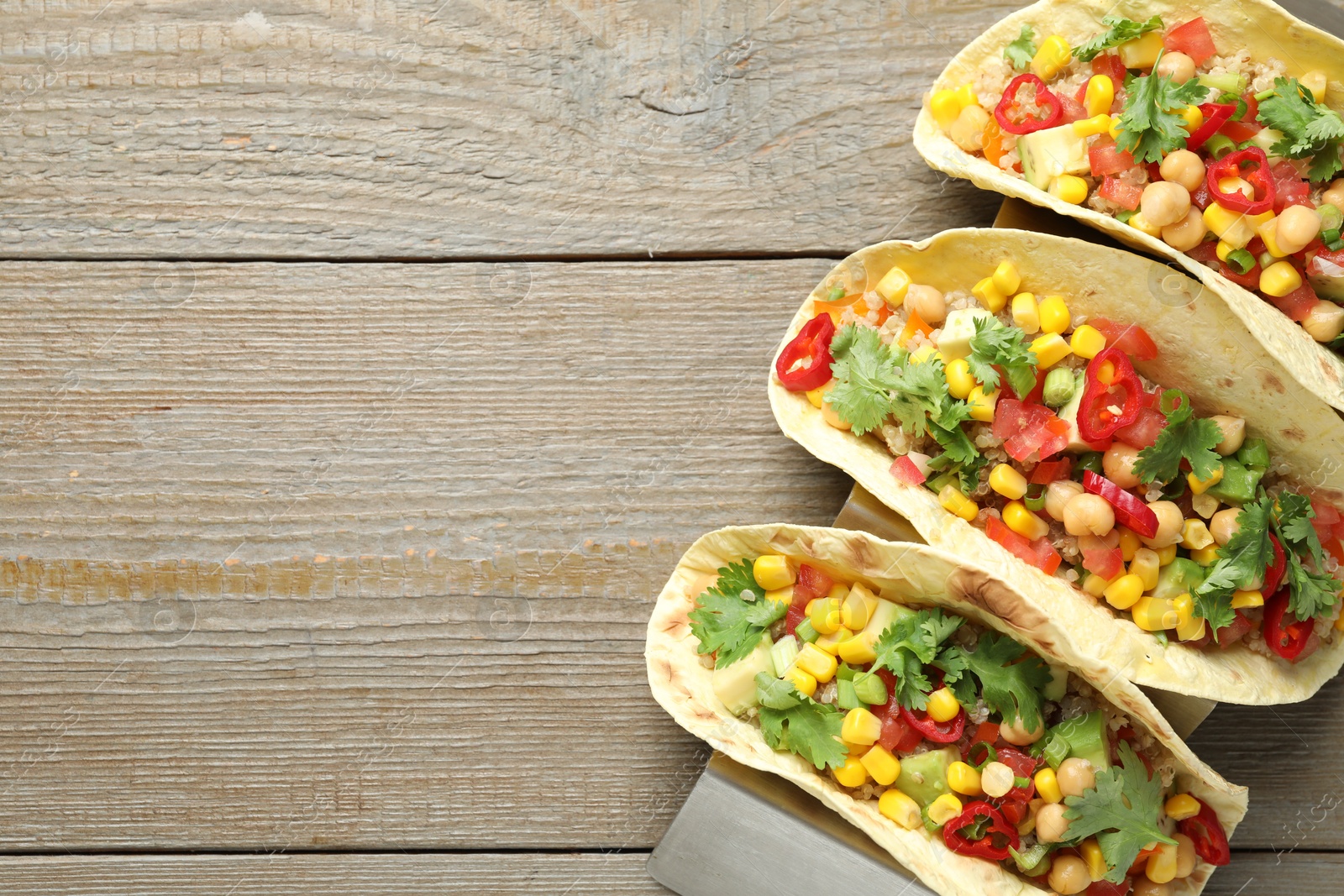 Photo of Tasty vegetarian tacos with chickpeas, corn and quinoa served on wooden table, top view. Space for text