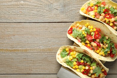 Photo of Tasty vegetarian tacos with chickpeas, corn and quinoa served on wooden table, top view. Space for text