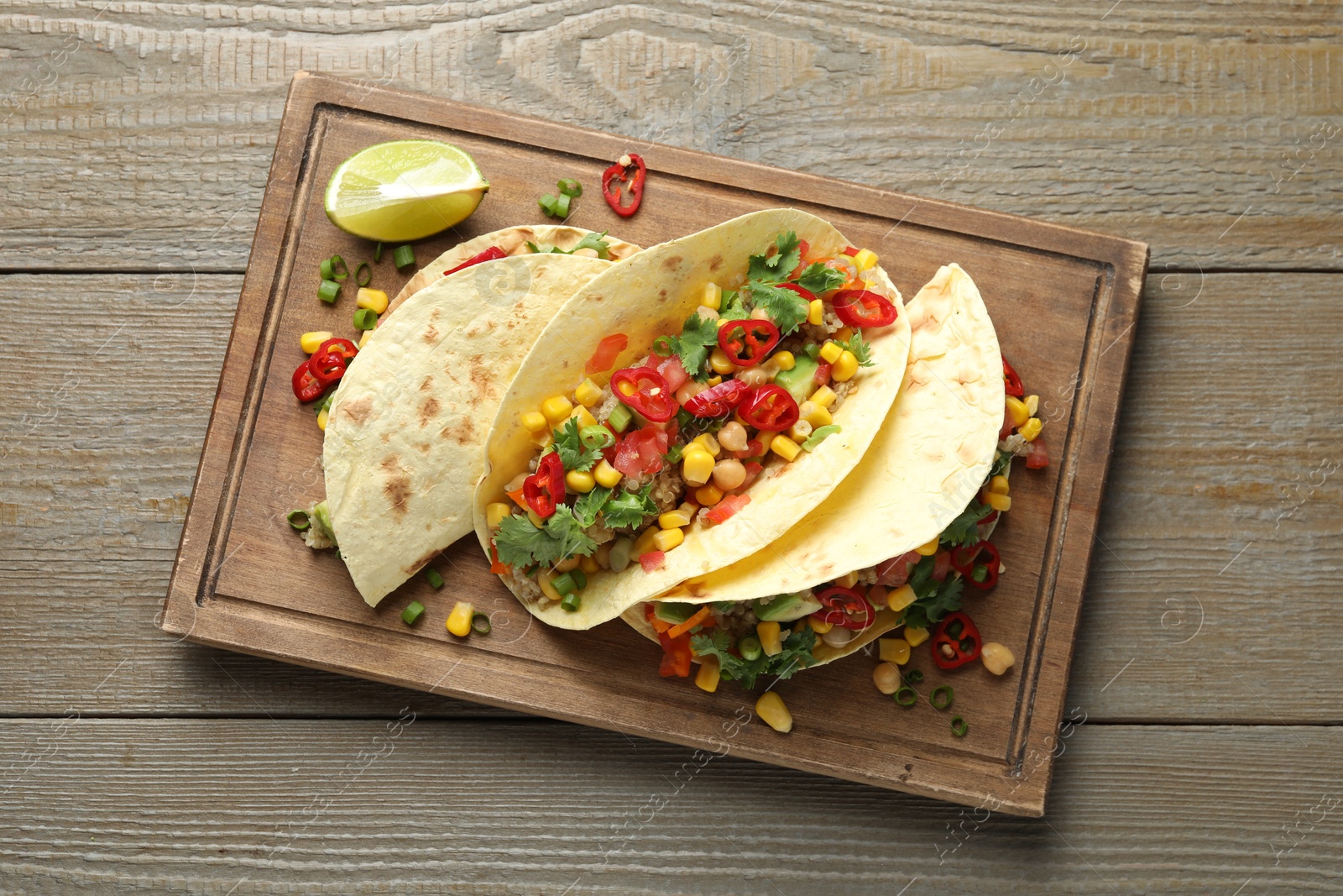 Photo of Tasty vegetarian tacos with chickpeas, corn and quinoa served on wooden table, top view
