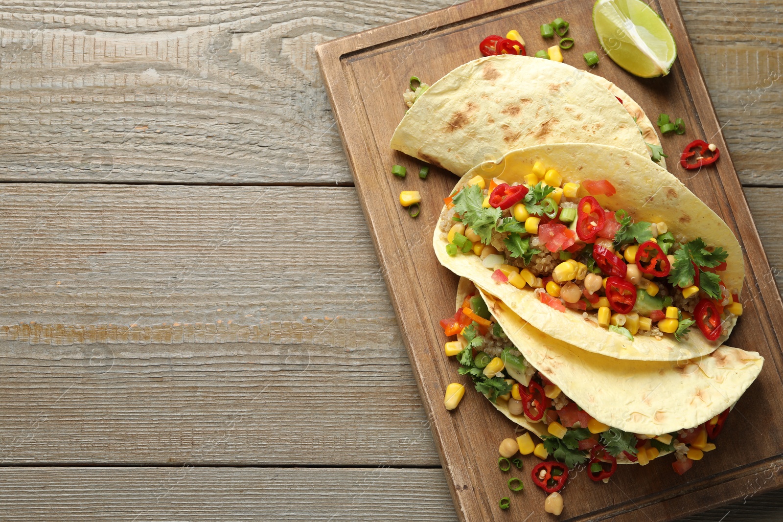 Photo of Tasty vegetarian tacos with chickpeas, corn and quinoa served on wooden table, top view. Space for text