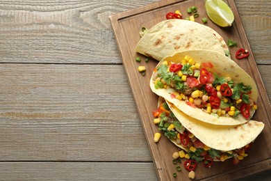 Photo of Tasty vegetarian tacos with chickpeas, corn and quinoa served on wooden table, top view. Space for text