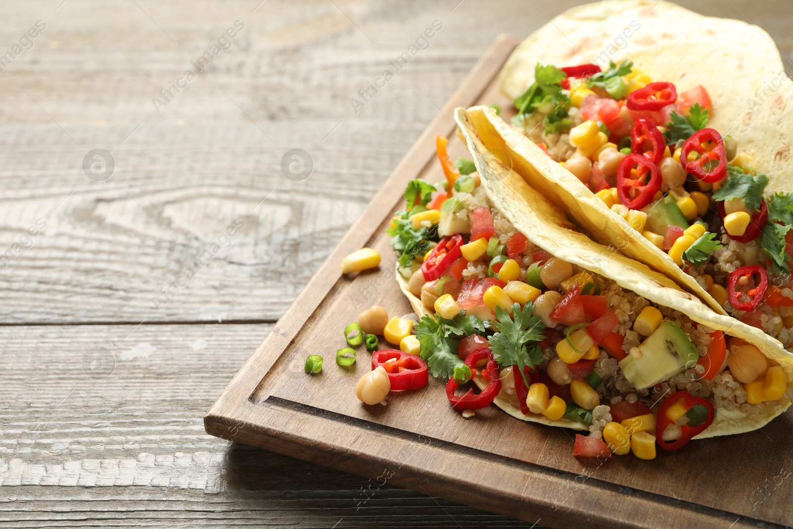 Photo of Tasty vegetarian tacos with chickpeas, corn and quinoa served on wooden table, closeup. Space for text