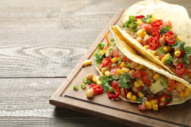 Photo of Tasty vegetarian tacos with chickpeas, corn and quinoa served on wooden table, closeup. Space for text