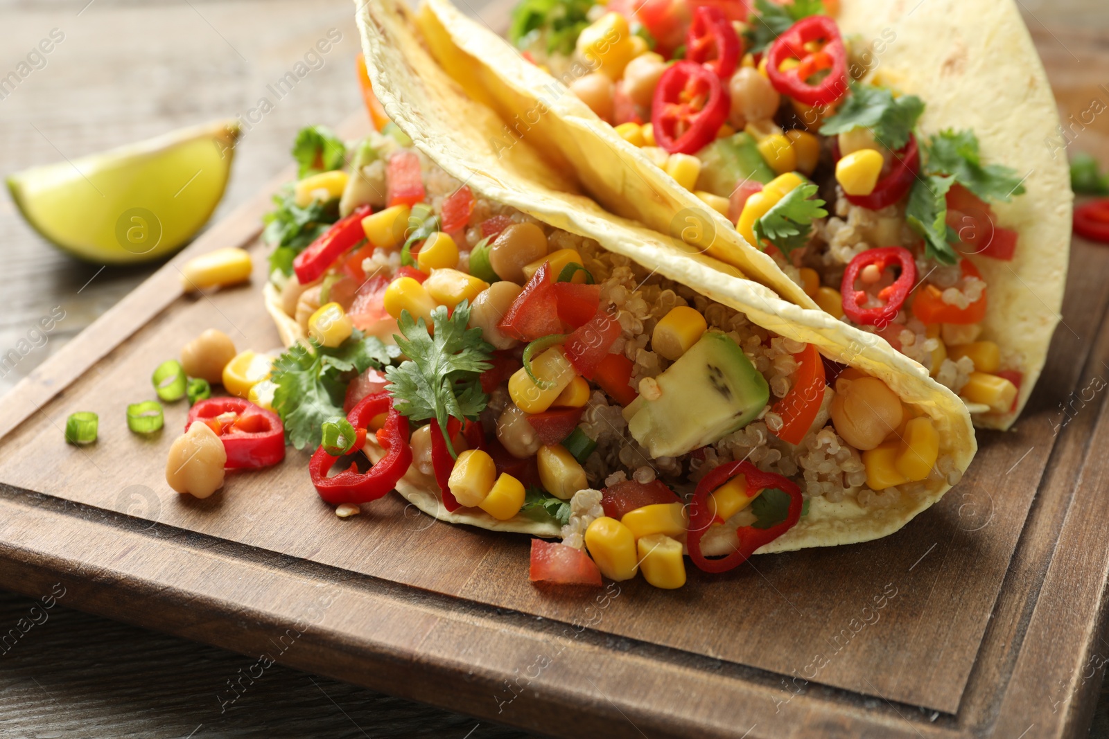Photo of Tasty vegetarian tacos with chickpeas, corn and quinoa served on wooden table, closeup