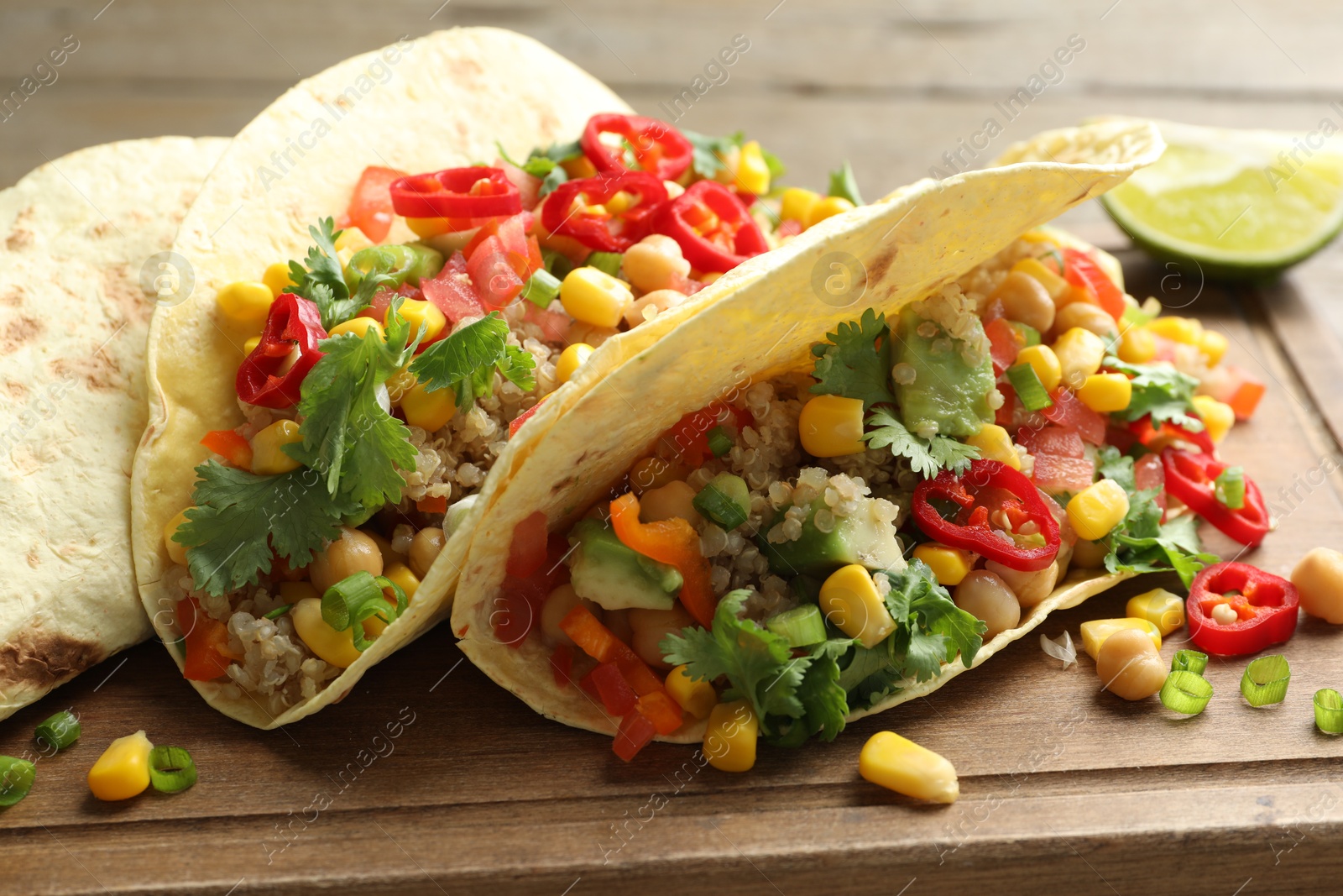 Photo of Tasty vegetarian tacos with chickpeas, corn and quinoa served on wooden table, closeup