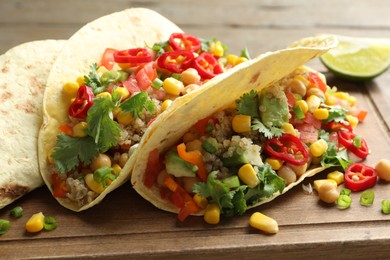 Photo of Tasty vegetarian tacos with chickpeas, corn and quinoa served on wooden table, closeup