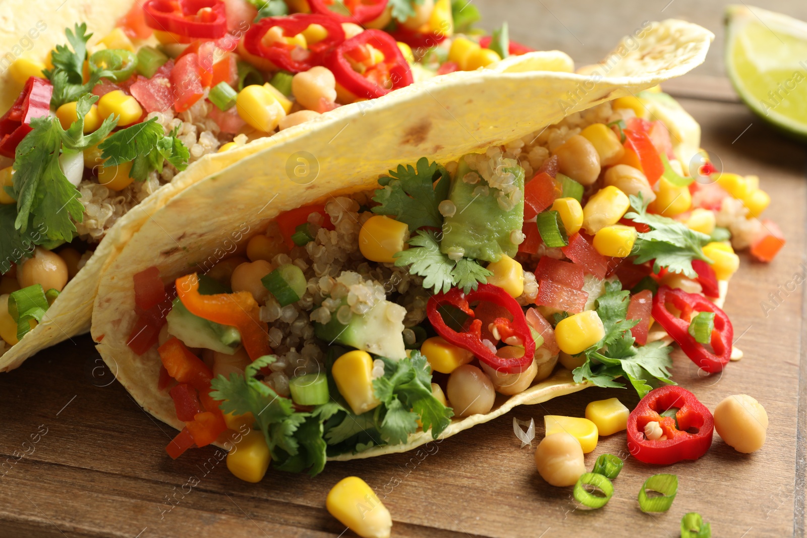 Photo of Tasty vegetarian tacos with chickpeas, corn and quinoa served on wooden table, closeup