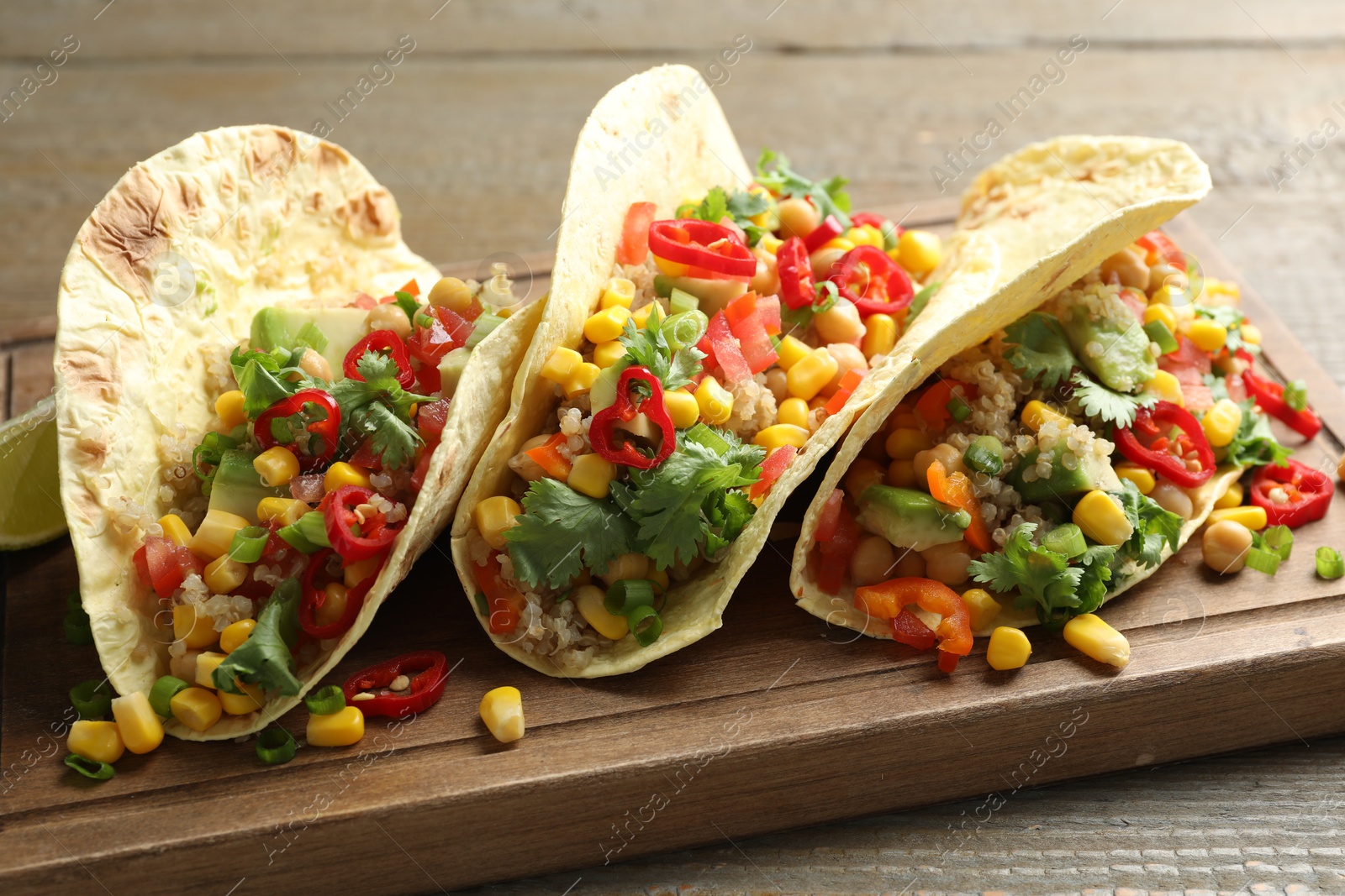 Photo of Tasty vegetarian tacos with chickpeas, corn and quinoa served on wooden table, closeup