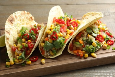 Photo of Tasty vegetarian tacos with chickpeas, corn and quinoa served on wooden table, closeup