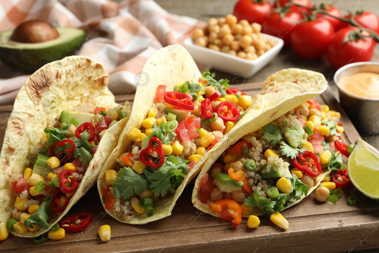 Photo of Tasty vegetarian tacos with chickpeas, corn and quinoa served on wooden table, closeup