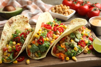 Photo of Tasty vegetarian tacos with chickpeas, corn and quinoa served on wooden table, closeup