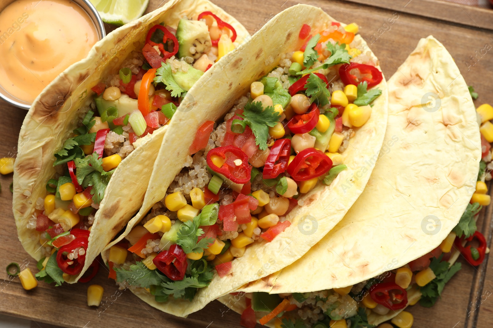 Photo of Tasty vegetarian tacos with chickpeas, corn and quinoa served on wooden table, top view