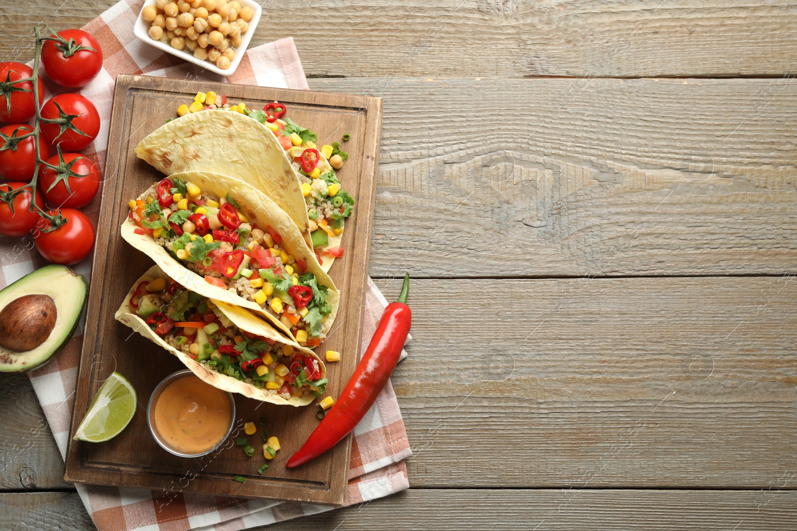 Photo of Tasty vegetarian tacos with chickpeas, corn and quinoa served on wooden table, flat lay. Space for text