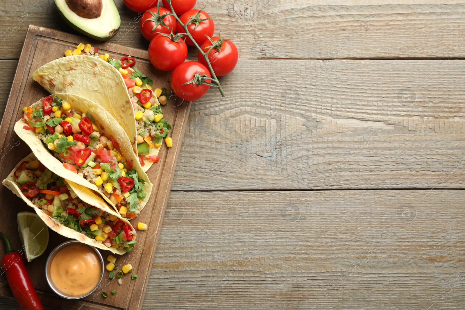 Photo of Tasty vegetarian tacos with chickpeas, corn and quinoa served on wooden table, flat lay. Space for text