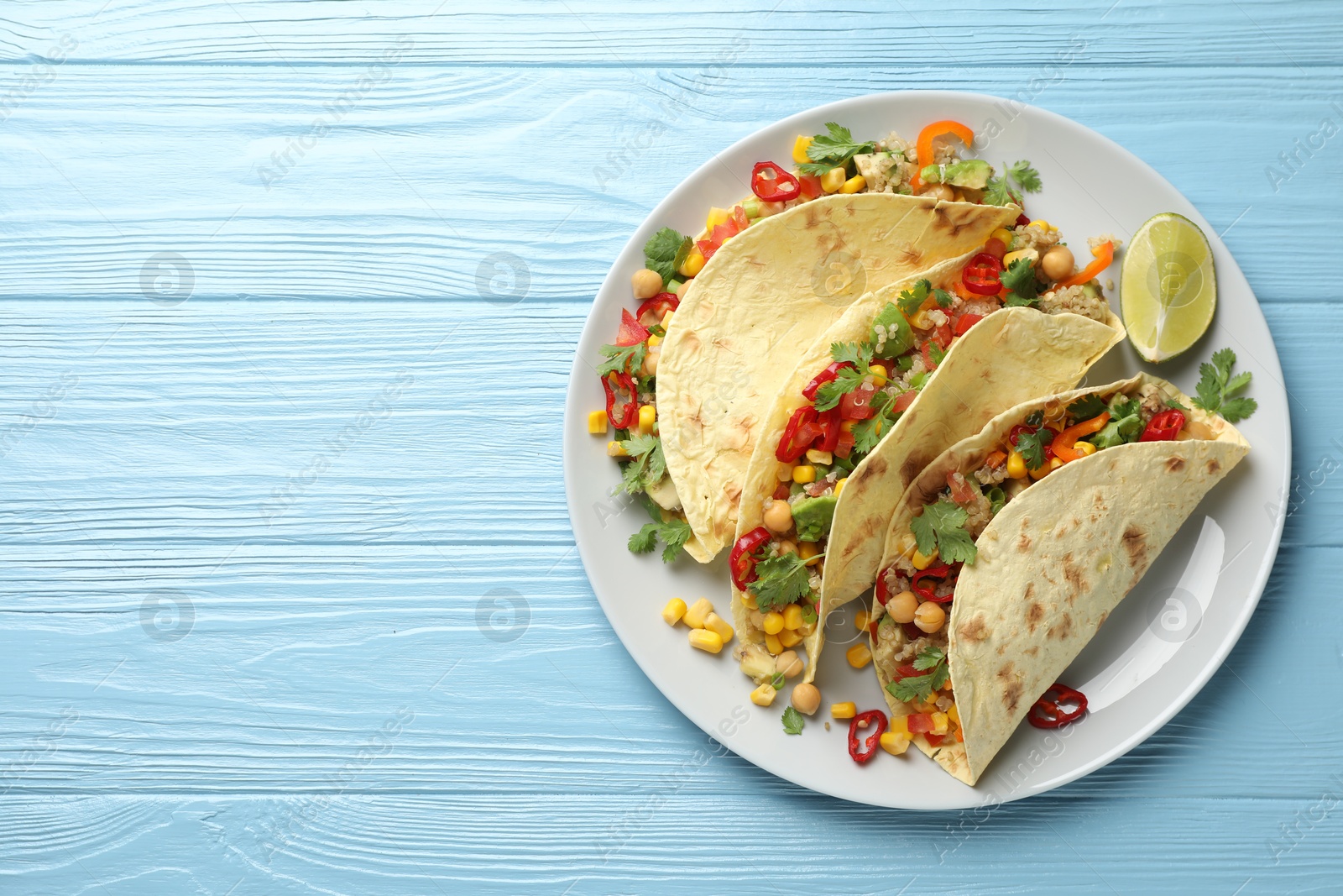 Photo of Tasty vegetarian tacos with chickpeas, corn and quinoa served on light blue wooden table, top view. Space for text