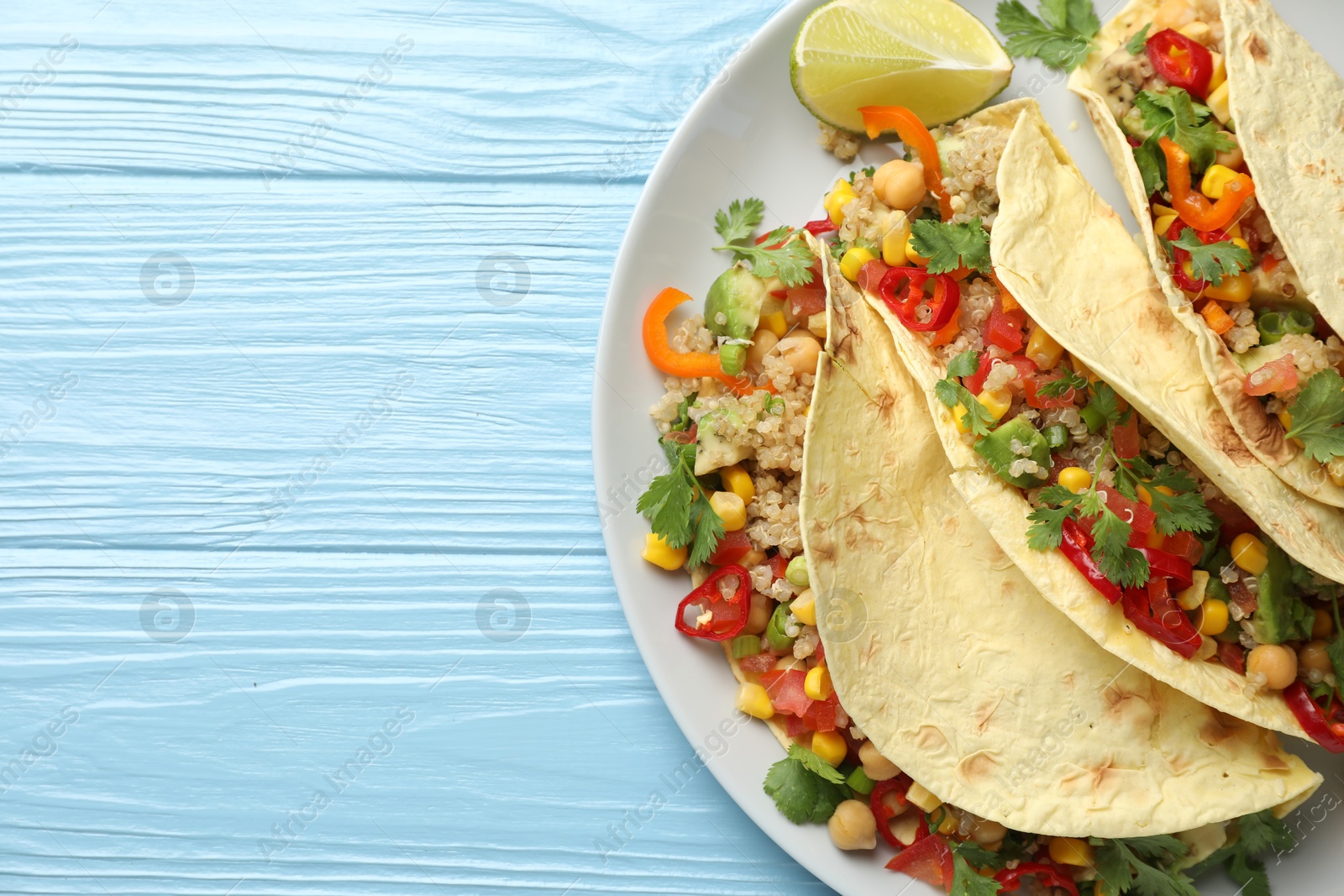 Photo of Tasty vegetarian tacos with chickpeas, corn and quinoa served on light blue wooden table, top view. Space for text