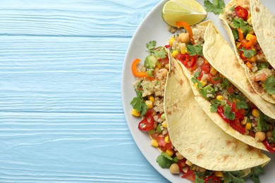 Photo of Tasty vegetarian tacos with chickpeas, corn and quinoa served on light blue wooden table, top view. Space for text
