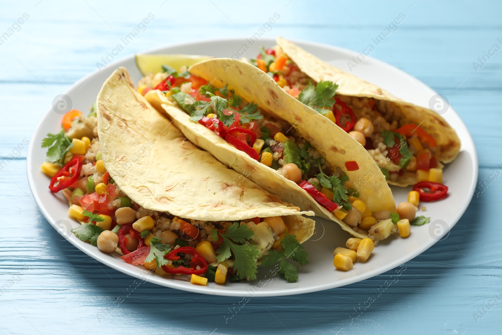 Photo of Tasty vegetarian tacos with chickpeas, corn and quinoa served on light blue wooden table, closeup