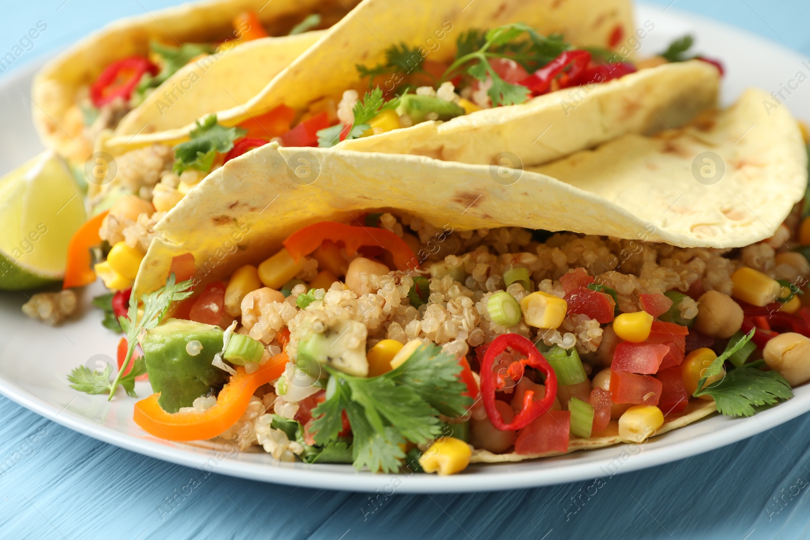 Photo of Tasty vegetarian tacos with chickpeas, corn and quinoa served on light blue wooden table, closeup