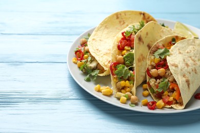 Photo of Tasty vegetarian tacos with chickpeas, corn and quinoa served on light blue wooden table, closeup. Space for text