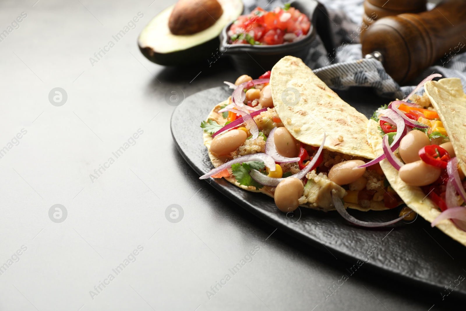 Photo of Tasty vegetarian tacos with beans and quinoa served on grey table, closeup. Space for text