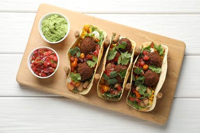Photo of Tasty vegetarian tacos with falafel served with salsa and guacamole on white wooden table, top view