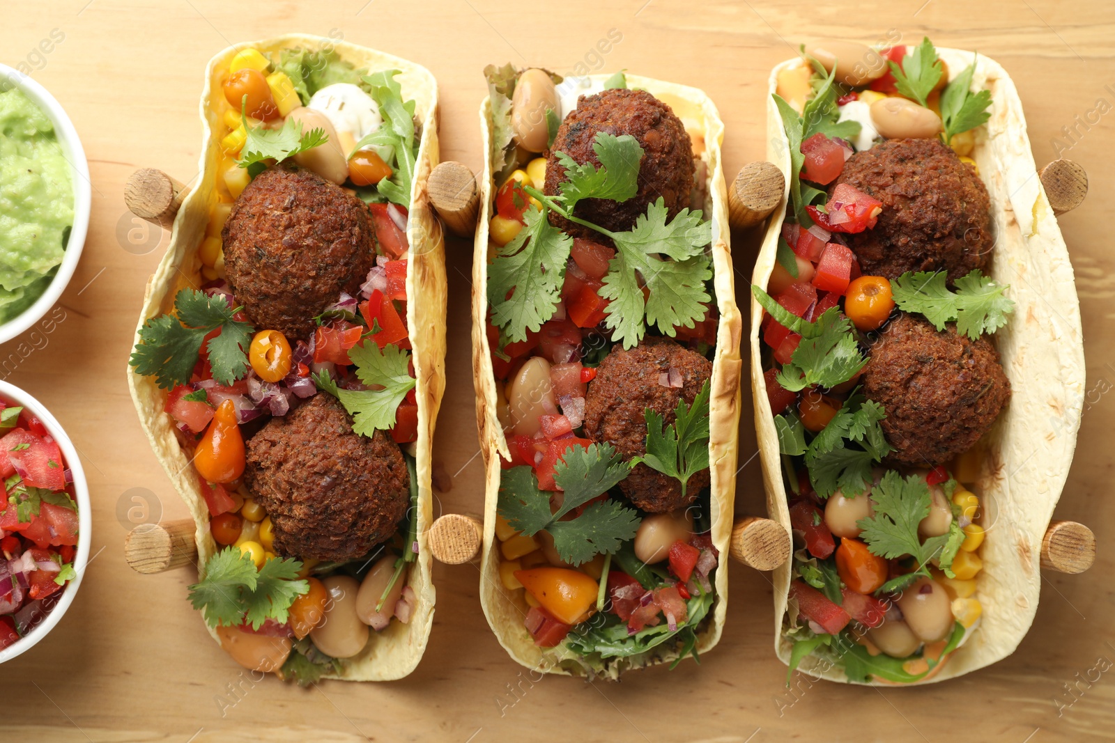 Photo of Tasty vegetarian tacos with falafel served with salsa and guacamole on wooden board, flat lay