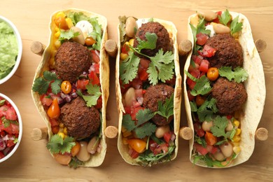 Photo of Tasty vegetarian tacos with falafel served with salsa and guacamole on wooden board, flat lay