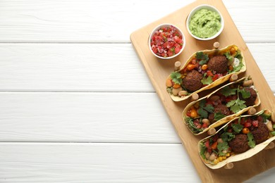 Photo of Tasty vegetarian tacos with falafel served with salsa and guacamole on white wooden table, top view. Space for text