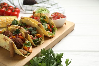 Photo of Tasty vegetarian tacos with falafel served with salsa and guacamole on white wooden table, closeup. Space for text
