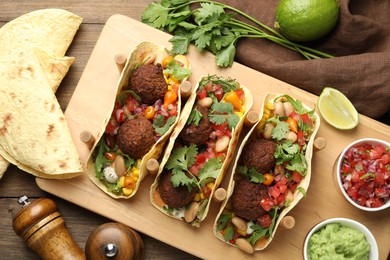 Photo of Tasty vegetarian tacos with falafel served with salsa and guacamole on wooden table, flat lay