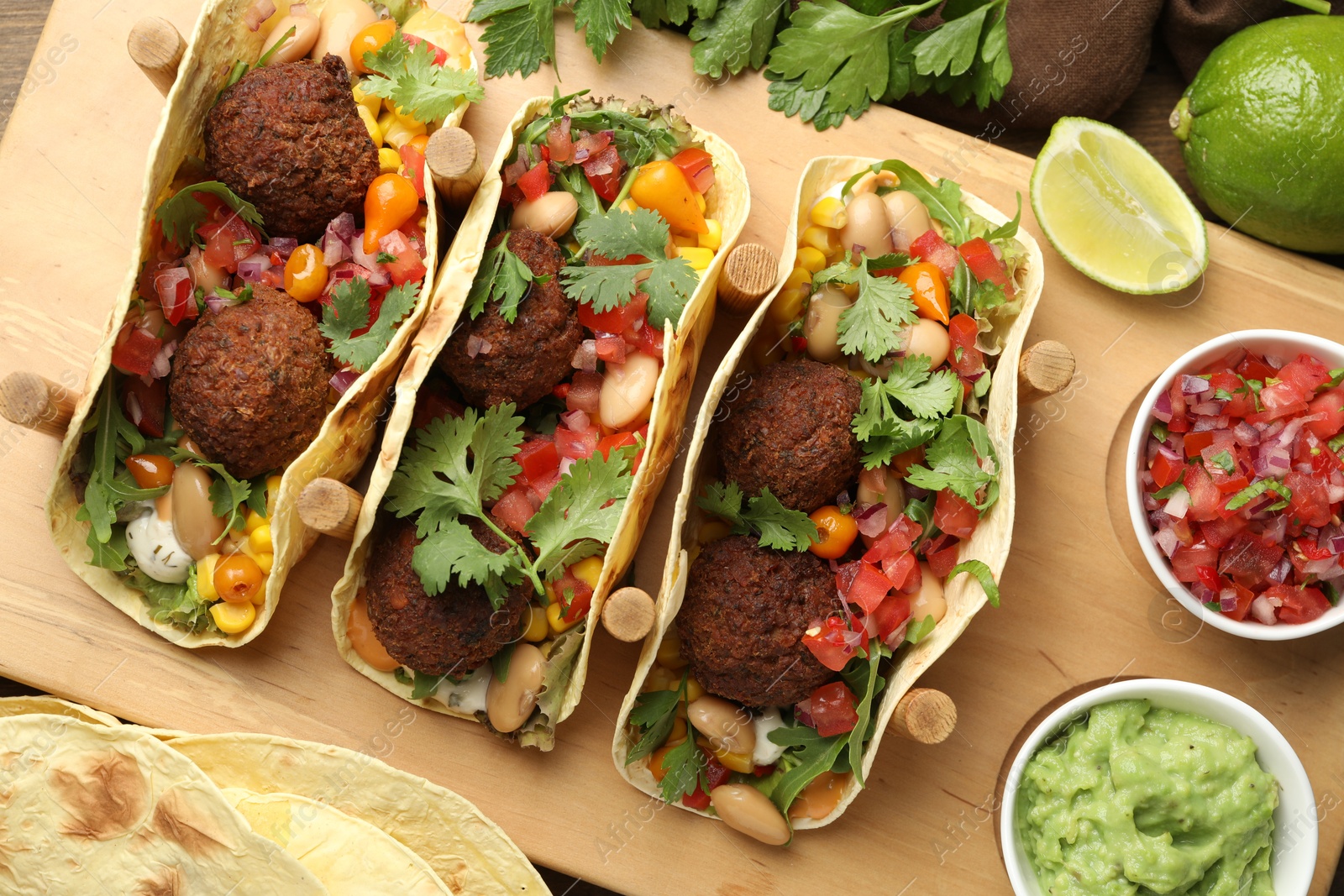 Photo of Tasty vegetarian tacos with falafel served with salsa and guacamole on wooden table, flat lay