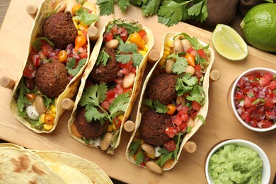 Photo of Tasty vegetarian tacos with falafel served with salsa and guacamole on wooden table, flat lay