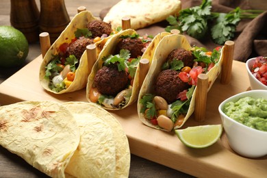 Photo of Tasty vegetarian tacos with falafel served with salsa and guacamole on wooden table, closeup